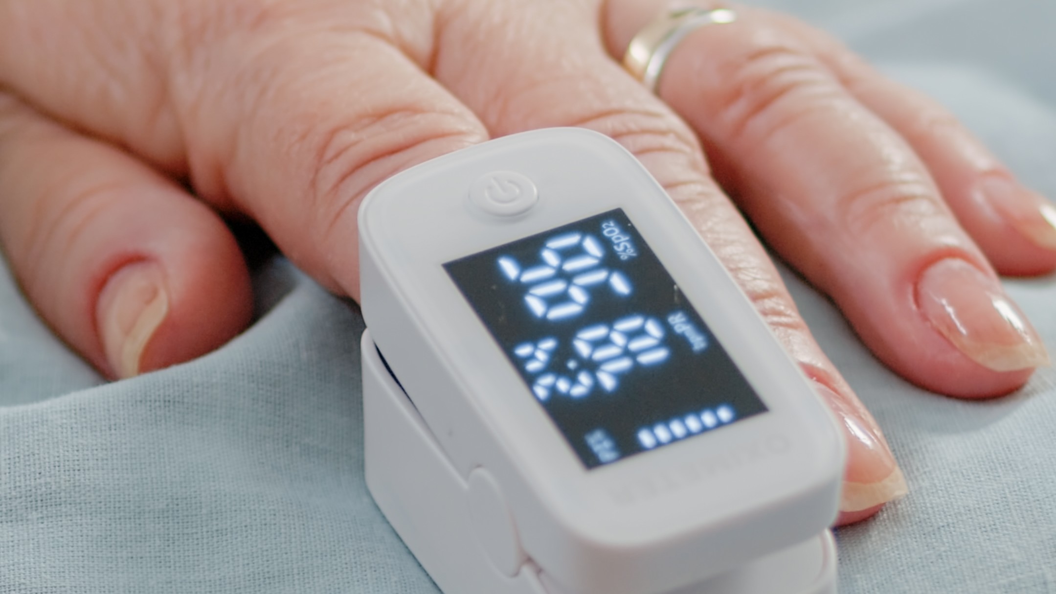 Close up of hand of aged patient with oximeter in bed
